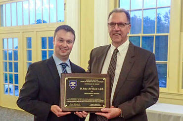 Two men standing next to each other while holding a wood and metal plaque award smiling for the camera.