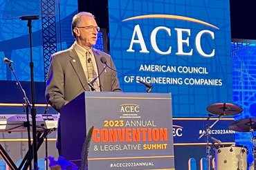 a man on stage standing behind a podium and speaking.