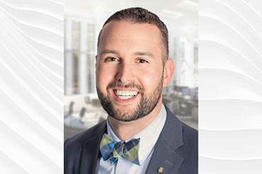 Jeremy wearing a gray suit, light blue shirt with a bow tie smiling for the camera.