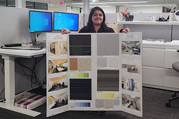 A women with dark hair standing in an office holding a project poster board.