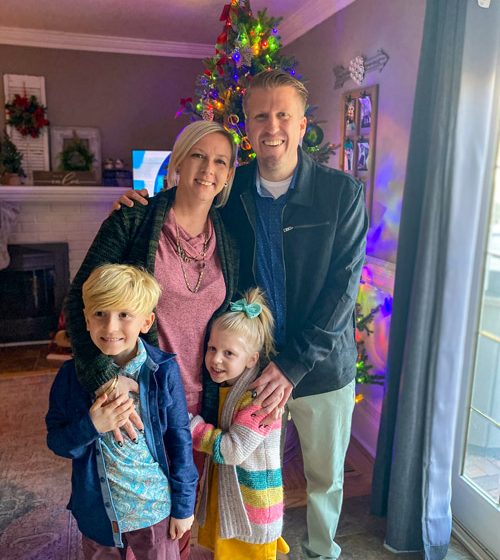 A woman, a man, and two children stand in front of a Christmas tree.