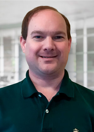 A man wearing a dark polo shirt and smiling at the camera.