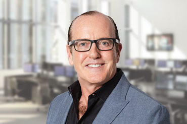 Man wearing glasses and a gray suit smiles for a portrait.