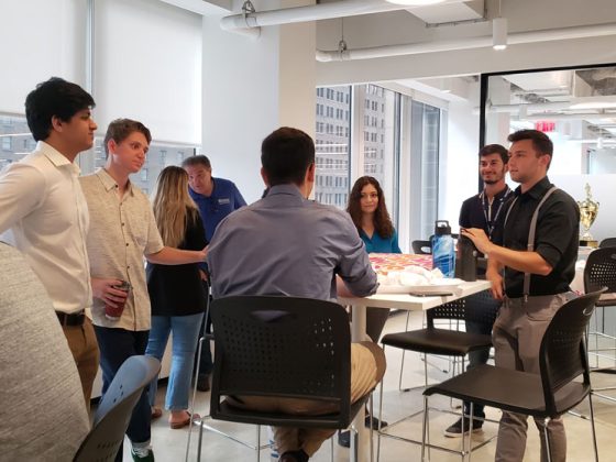 A group of Gannett Fleming employees and interns gather in a break room to eat donuts and network.