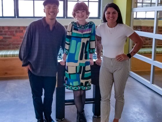 Three diverse Gannett Fleming employees and interns smile at the camera in a modern office.