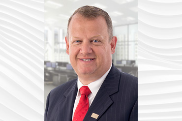 Smiling man wearing a white shirt, red tie, and blue pinstripe suit.