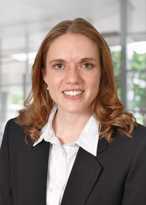 A woman with light brown hair wearing a white shirt and dark suit jacket smiling for the camera.