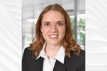 A woman with light brown hair wearing a white shirt and dark suit jacket smiling for the camera.