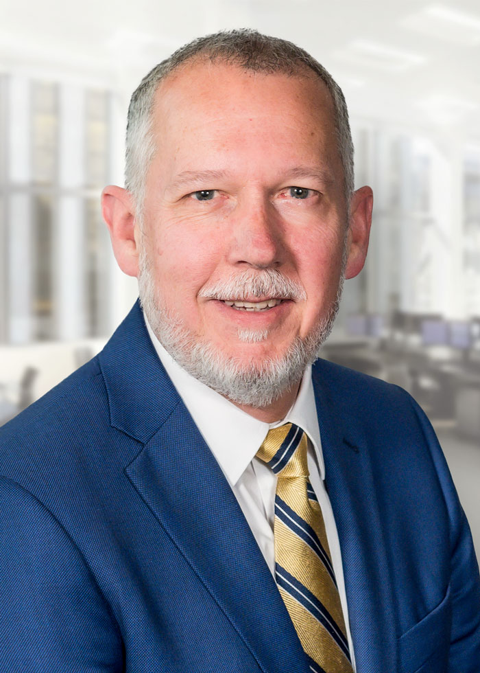 Art wearing a blue suit jacket, a white shirt with a gold and blue striped tie smiling for the camera.