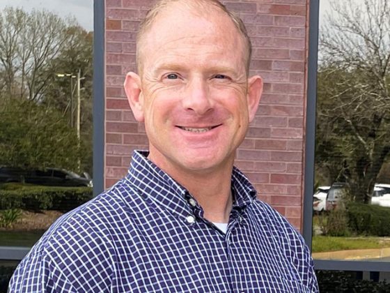 A Caucasian man in blue plaid button-down shirt smiles outdoors for a picture.