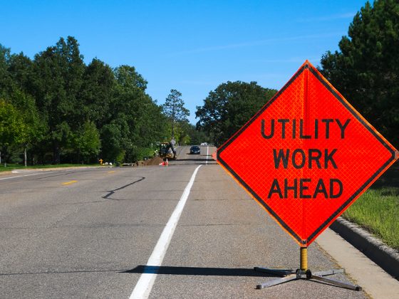 An orange utility sign reading "Utility work ahead" on the side of a two-way street.