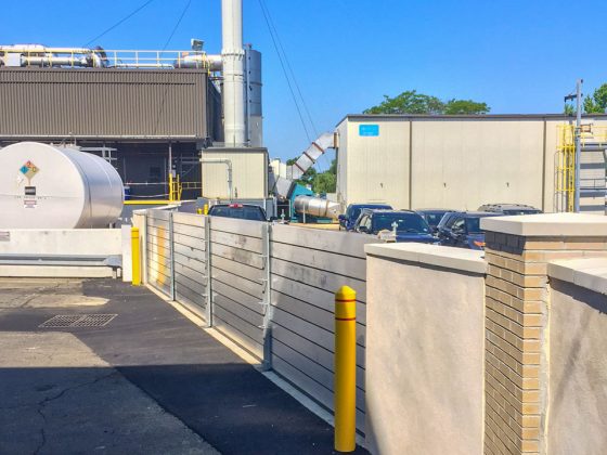 A floodwall with aluminum panels next to a parking lot on a sunny day.