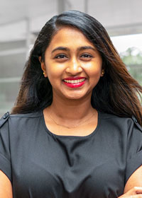 A woman with dark hair wearing a dard gray shirt smiling for the camera.