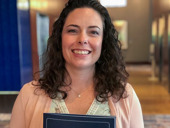 A dark curly-haired female smiles while holding a college commencement program booklet.