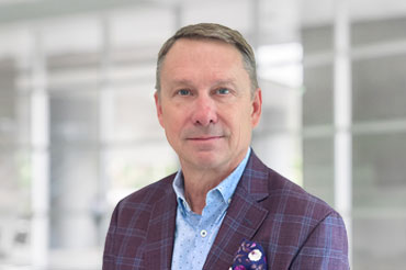 A businessman wearing a plum-colored sports coat with a floral pocket square poses for a professional headshot.