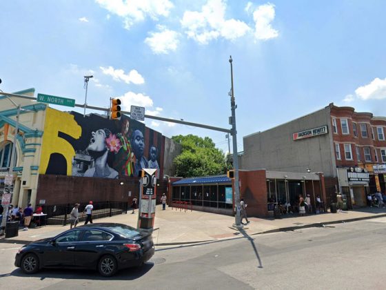 The intersection of a road with a subway sign and a colorful mural on a brick exterior. The exterior of the Penn-North Metro SubwayLink Station, shown here, received upgrades to its lighting, sidewalks, and architectural appearance.