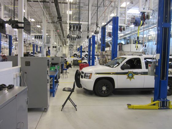 A white police vehicle is parked in the Pima County Fleet Maintenance Facility. Large equipment is on the floor and hangs from the ceiling.