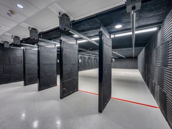 Five shooting bays facing a bullet trap in a range with black armored walls and a white concrete floor.