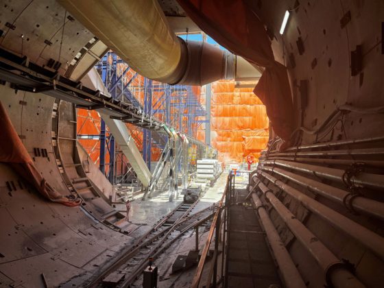 A large tunnel opening with construction equipment, rail tracks, and metal framing.