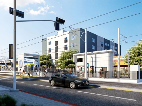 Black car driving down street near East San Fernando Valley LRT station while people walk along sidewalk