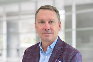 A businessman wearing a plum-colored sports coat with a floral pocket square poses for a professional portrait.